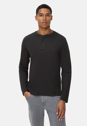 Black long-sleeve henley shirt with three-button placket, soft texture, and ribbed neckline. Model pairs with light gray jeans.