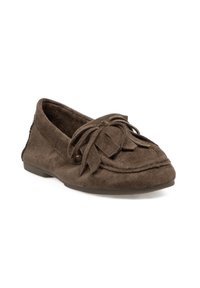 Mocasin de ante marrón con suela plana, que presenta un detalle de lazo y acentos de flecos en la zona del dedo, diseñado para la comodidad y flexibilidad.