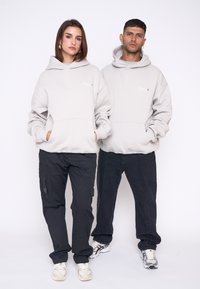 Des sweat-shirts gris clair avec de grandes poches avant, portés avec un pantalon noir. Les sweat-shirts présentent un logo brodé subtil sur la poitrine.