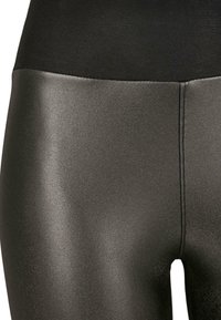 Leggings noirs taille haute en tissu brillant et extensible. Texture lisse avec un éclat subtil et des coutures renforcées le long des coutures.