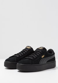 Scarpe sneakers platform in suede nero con suole in gomma testurizzata, caratterizzate da allacciatura frontale e dettagli in oro sul linguetta e sul lato.