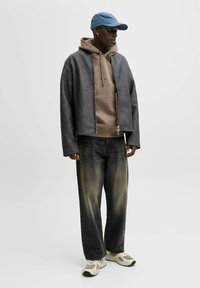 Μαύρο δερμάτινο μπουφάν με γκρι φούτερ από μέσα, συνδυασμένο με ξεβαμμένο μαύρο τζιν και ανοιχτόχρωμα αθλητικά παπούτσια. Περιλαμβάνονται μπλε καπέλο και σκουλαρίκια.