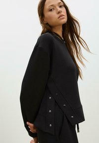 Czarna bluza z luźnym krojem,oversized rękawami, detalami z napami po bokach oraz miękkim, teksturowanym materiałem.