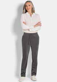 Grijze, trekkoordbroeken van zachte stof, ontworpen met een ontspannen pasvorm. Gemaakt in combinatie met een witte blouse en witte sneakers.