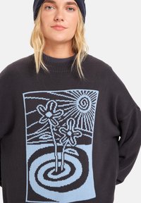Svart strikkegenser med en lyseblå grafikk av blomster og spiraler, rund halslinning og avslappet passform.