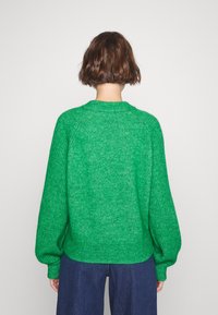 Grön stickad tröja med en texturerad, fluffig finish. Har en rund halsringning, långa ballongsärmar och en avslappnad passform. Mjuk, varm material.