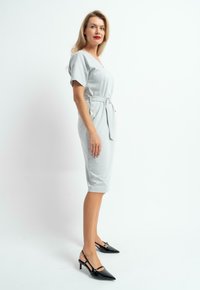 Jasnoszara sukienka z krótkimi rękawami, z paskiem w talii, o długości do kolan, połączona z czarnymi butami typu slingback na szpilce. Gładka faktura materiału.