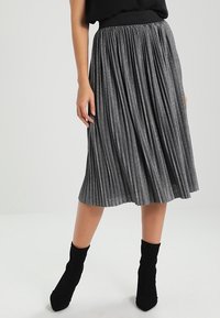 Plisovaná midi sukně v metalické šedé tkanině; má elastický pas a sahá pod kolena, stylizováno s černými kotníkovými botami.