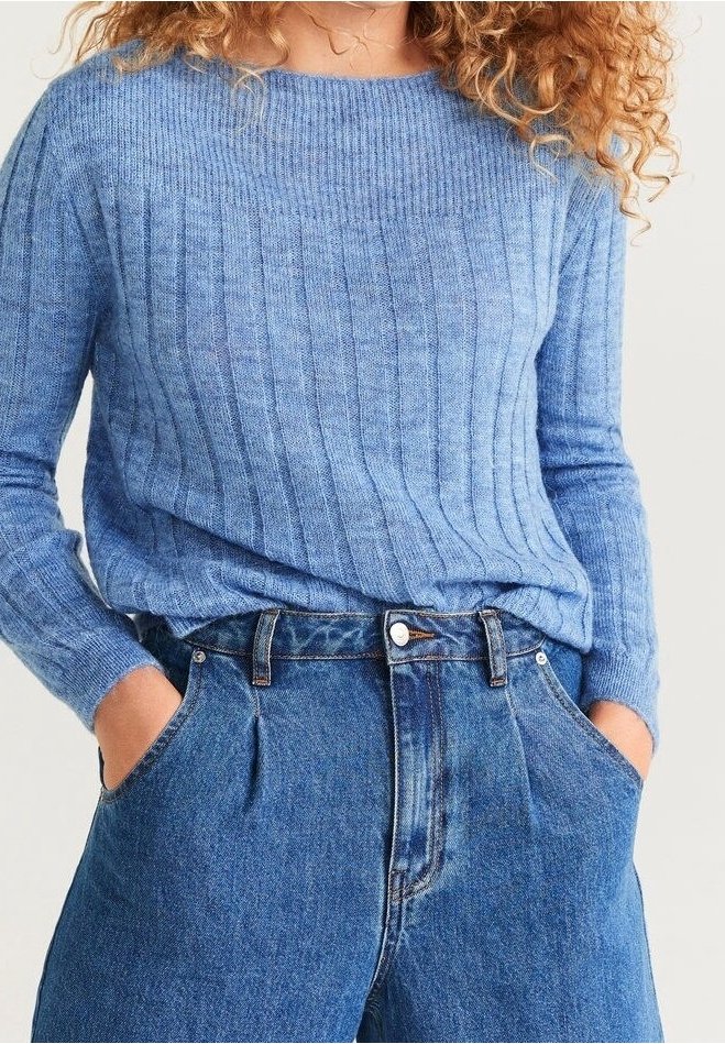 Jasnoniebieski sweter z prążkowanej wełny o okrągłym dekolcie, zestawiony z dżinsami o wysokim stanie, luźnymi w kroju, z przody z fałdami i kieszeniami.