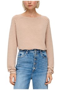 Maglietta beige a maniche lunghe con scollatura rotonda; abbinata a jeans azzurri a vita alta con chiusura a bottoni e dettagli strappati.