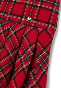 Roter Karorock mit Falten, schwarzen und gelben Akzenten sowie einem kleinen silbernen Herzlogo am Bündchen. Aus Baumwollmaterial.