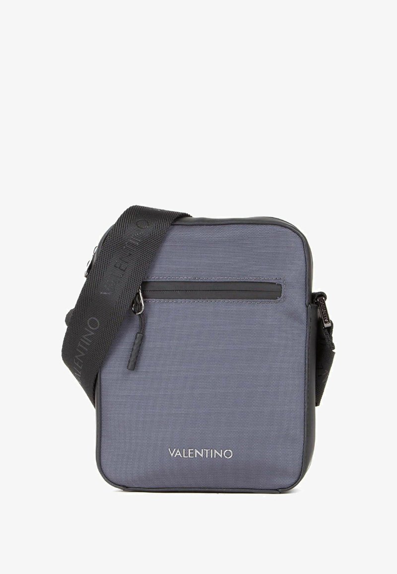 Sac bandoulière en nylon gris avec une poche avant zippée, une sangle noire réglable et un logo embossé sur le bas avant.