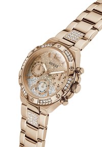 Montre Guess en or rose avec accents en cristal, cadran scintillant, trois sous-cadrans pour les fonctions 24 heures, date et jour de la semaine.