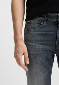 Vaqueros de mezclilla gris oscuro con un ajuste slim, que cuentan con bolsillos frontales, un sutil desvanecimiento y una pequeña etiqueta de la marca cerca de la cinturilla.