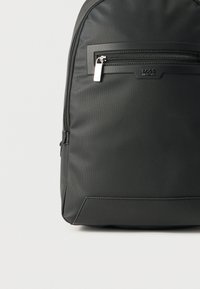 Μαύρο υφασμάτινο σακίδιο με μπροστινή τσέπη με φερμουάρ, που διαθέτει ασημένιο τράβηγμα φερμουάρ και μικρό λογότυπο BOSS σε απλό φωτεινό φόντο.