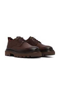 Een paar donkerbruin leren veterschoenen met dikke, textuur rubberen zolen op een witte achtergrond.
