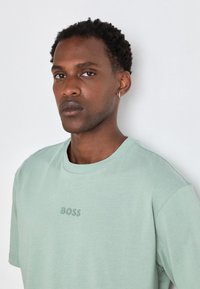 Mintgrønn T-skjorte laget av bomull, med rund hals, korte ermer, og preget "BOSS"-logo på brystet. Glatt tekstur.