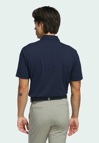 Granatowa koszulka polo z krótkim rękawem i kołnierzykiem, zestawiona z jasnoszarymi spodniami. Posiada subtelną teksturę i małe logo na spodniach.