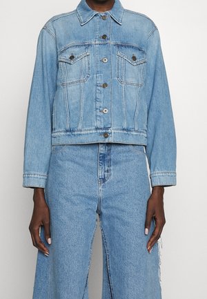 Person iført lyseblå cropped denimjakke med knaplukning og højttaljede vidde jeans i denim.