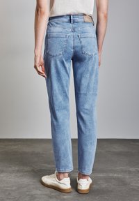 Jeans de mezclilla azul claro con un corte recto, cinco bolsillos y una etiqueta de cuero en la parte trasera de la cinturilla. Llevados con zapatillas blancas.