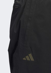 Shorts de sport noirs avec une texture lisse, une poche sur le côté, et le logo Adidas en vert olive sur le bas.