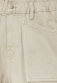 Primo piano di pantaloni in denim beige che mostrano la tasca anteriore, il passante per cintura, i dettagli delle cuciture e il bottone metallico etichettato "PULL&BEAR DENIM".