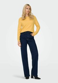 Yellow sweater with long sleeves, paired with dark blue wide-leg jeans. Black heeled shoes, smooth texture, and minimalistic design.