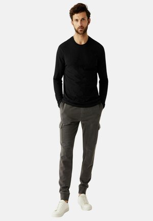 Maglietta nera a maniche lunghe abbinata a pantaloni cargo grigi con tasche laterali e sneakers bianche; design e vestibilità semplici e casual.