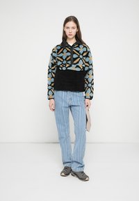 Patterned fleece pullover in black, blue, and orange, paired with light blue striped jeans and gray sneakers; features a half-button collar.
