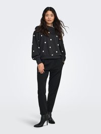 Black sweatshirt with white floral patterns, relaxed fit, and balloon sleeves, paired with black trousers and stiletto ankle boots.