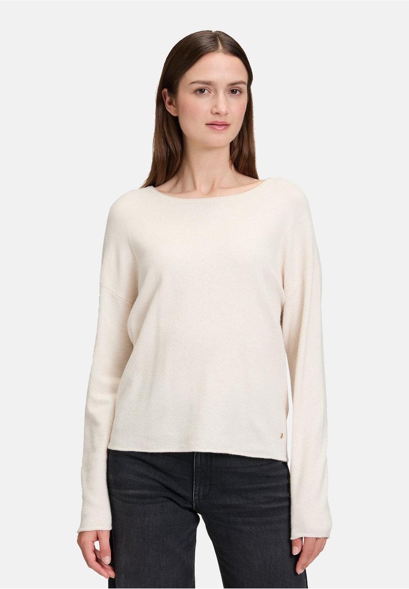 Jasno beżowy sweter z długim rękawem, okrągłym dekoltem i luźnym krojem. Teksturowany materiał, prosty krój oraz małe logo akcentowe na dole.