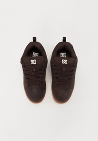Braune Wildleder-Sneaker mit gepolstertem Kragen, flachen Schnürsenkeln und einer Gummisohle. Mit einem Logo auf der Zunge und der Seite.