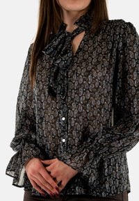 Blusa negra transparente con estampado de paisley, con un lazo en el cuello, botones en la parte delantera y mangas largas voluminosas con puños con volantes.