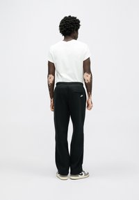 Čierne tepláky s elastickým pásom a bočným vreckom, skombinované s bielym tričkom s krátkym rukávom. Model otočený chrbtom, má na nohách sivé a biele topánky.