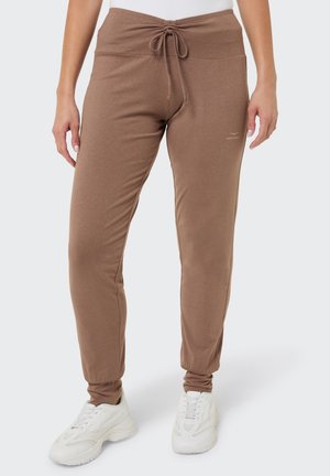 Braune, verjüngte Jogginghosen mit Kordelzug in der Taille, getragen mit weißen Sneakern und einem weißen Oberteil, gezeigt von der Taille bis zu den Füßen.