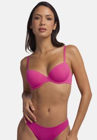 Soutien-gorge rembourré rose avec des bretelles réglables et une texture lisse. Présente un design de coque moulée et des côtés sans coutures pour une apparence élégante.