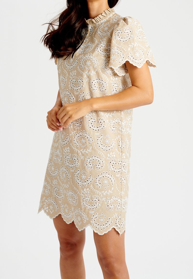 Beige klänning med blommig broderi, spetsig fåll och korta puffärmar. Tillverkad av textil med strukturerad yta och rynkad halsringning.