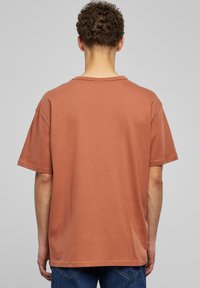 Kouřově hnědé bavlněné tričko s volným střihem, krátkými rukávy a kulatým výstřihem. Hladká textura, bez viditelných vzorů nebo kovových detailů.