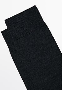 Schwarze knöchellange Socken mit einem gerippten, elastischen Bündchen. Hergestellt aus einem weichen, strukturierten Stoff, der durchgehend eine glatte Oberfläche aufweist.