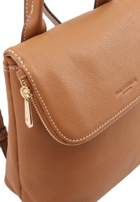 Bruine lederen handtas met een gestructureerde afwerking, een klepafsluiting, gouden ritsbeslag en contrasterende witte stiksels.