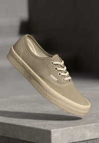 Beige auduma kedas ar teksturētu, krēmkrāsas gumijas zoli. Aprīkots ar baltām šņorēm un diegu. Noapaļota purngala un zemas formas dizains.