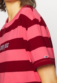 Striped t-shirt in pink and deep red, featuring a crew neck and short sleeves. Includes "Tommy Jeans" logo in silver on the front.