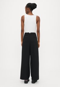 Μαύρο παντελόνι με φαρδιά μπατζάκια και ψηλή μέση, με τσέπες στο πίσω μέρος και V-σχήματος άνοιγμα στη μέση. Συνδυασμένο με λευκή μπλούζα.