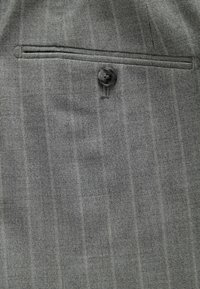Gray pinstriped fabric featuring a small pocket and a single black button. The texture appears smooth with a subtle sheen.
