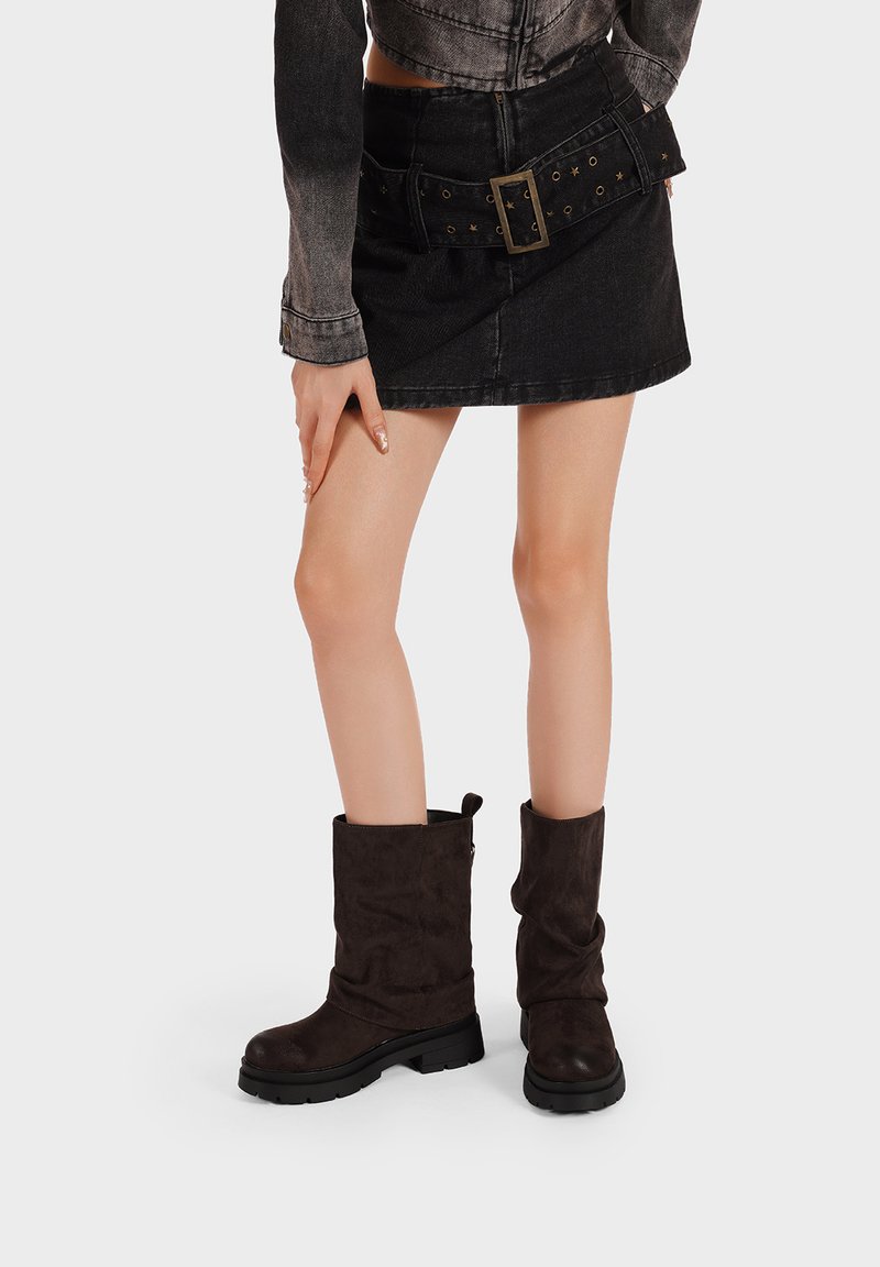 Stivali slouch in suede marrone con suola nera chunky. La parte superiore è dolcemente piegata, creando una silhouette rilassata.