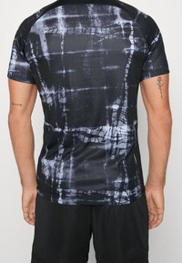 Camiseta deportiva negra con patrón abstracto gris, mangas cortas, textura suave y cuello redondo. Presenta un diseño ajustado y tela elástica.