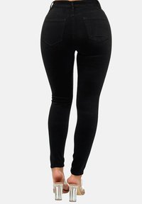Pantalones vaqueros negros ajustados de talle alto, hechos de denim elástico. Cuentan con dos bolsillos traseros y una silueta entallada. Se llevan sandalias de tacón transparente.