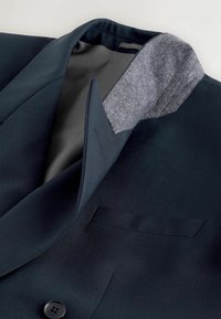 Blazer bleu marine foncé avec doublure de col en tissu gris, doublure intérieure noire et un seul bouton visible à l'avant.