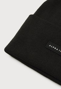 Black knit beanie featuring a folded cuff and a rectangular black label with white text "ALPHA INDUSTRIES". Soft texture and snug fit.