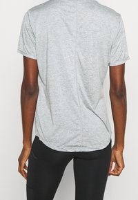 Grå kortärmad t-shirt med rund halsringning. Mjukt, texturerat tyg som har en mittsöm och lätt svansslut. Kombinerad med svarta leggings.